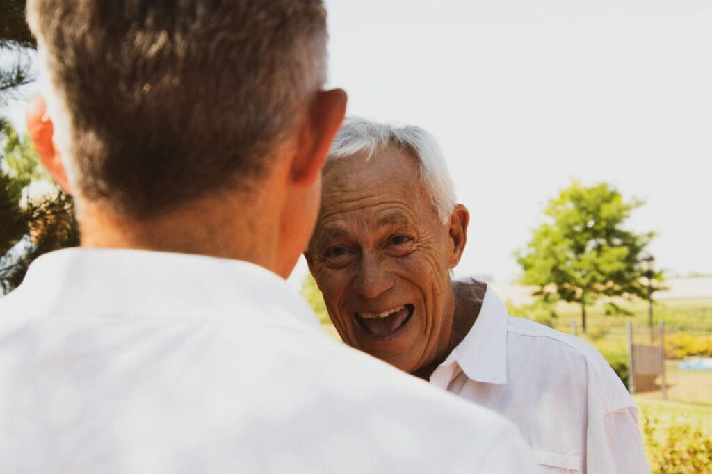 Älterer Mann lacht fröhlich in einem Gespräch im Freien.