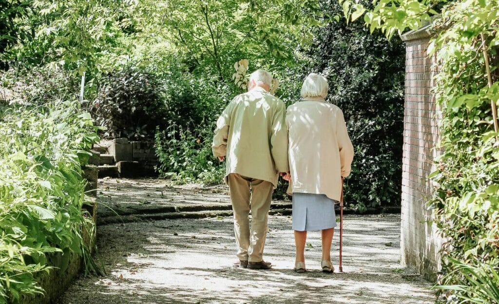 Älteres Paar spaziert Hand in Hand durch einen grünen Park.